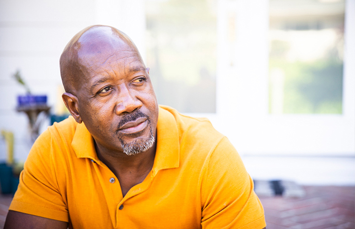 Man sitting on a bench outside with a wondering look on his face.